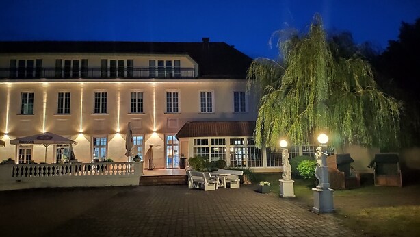 A large, well-lit building with a paved courtyard, outdoor seating area, and a large tree. - Hotel Der Lindenhof (Gotha)