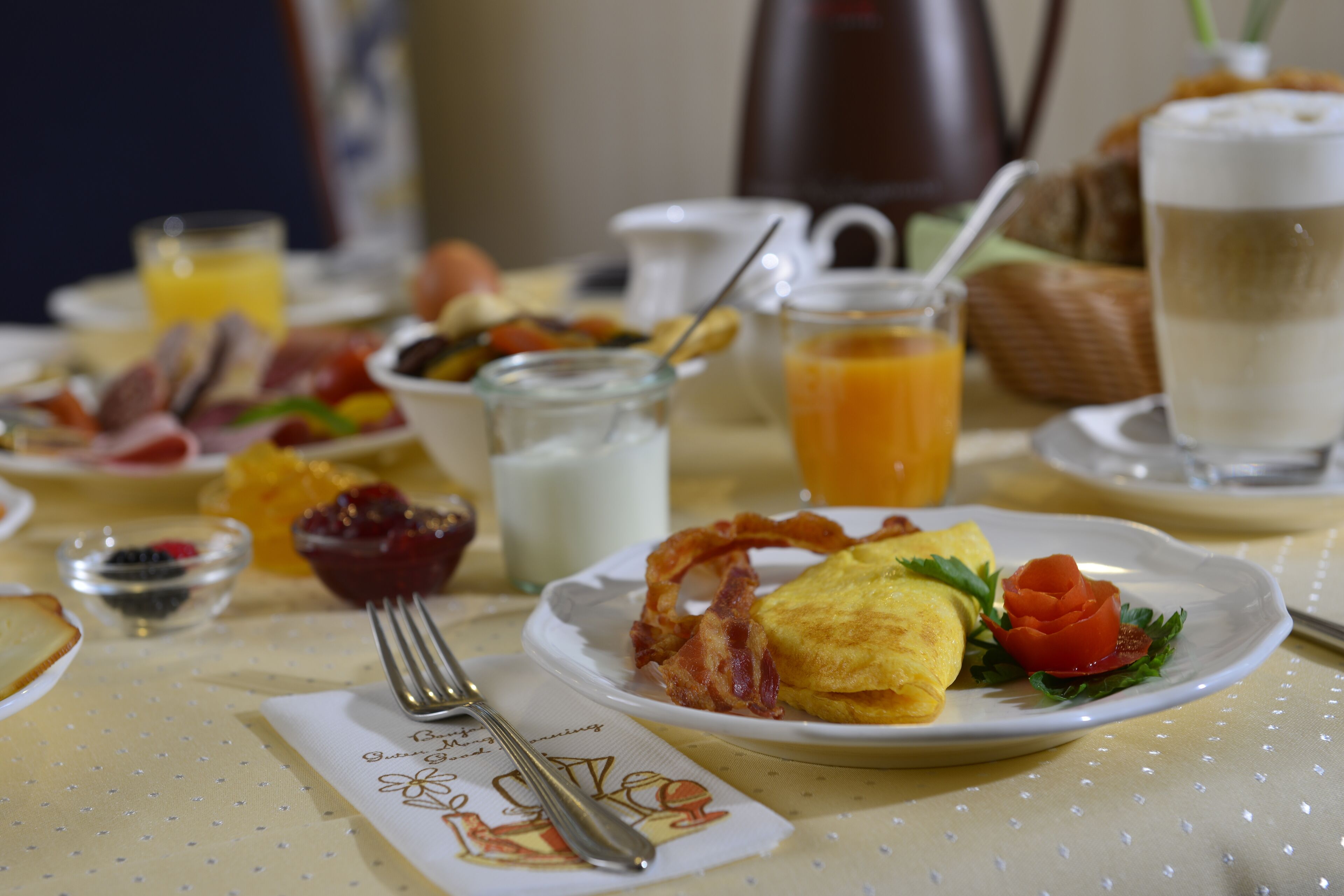 A breakfast table with plates of food, a coffee pot, and a glass of orange juice.