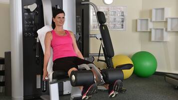 A woman using a leg press machine in a gym with exercise balls and a poster on the wall.