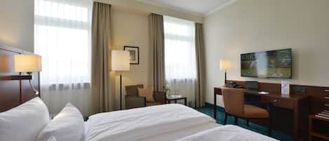 Habitación de hotel con dos camas, un escritorio, una silla, un televisor y una ventana con cortinas.