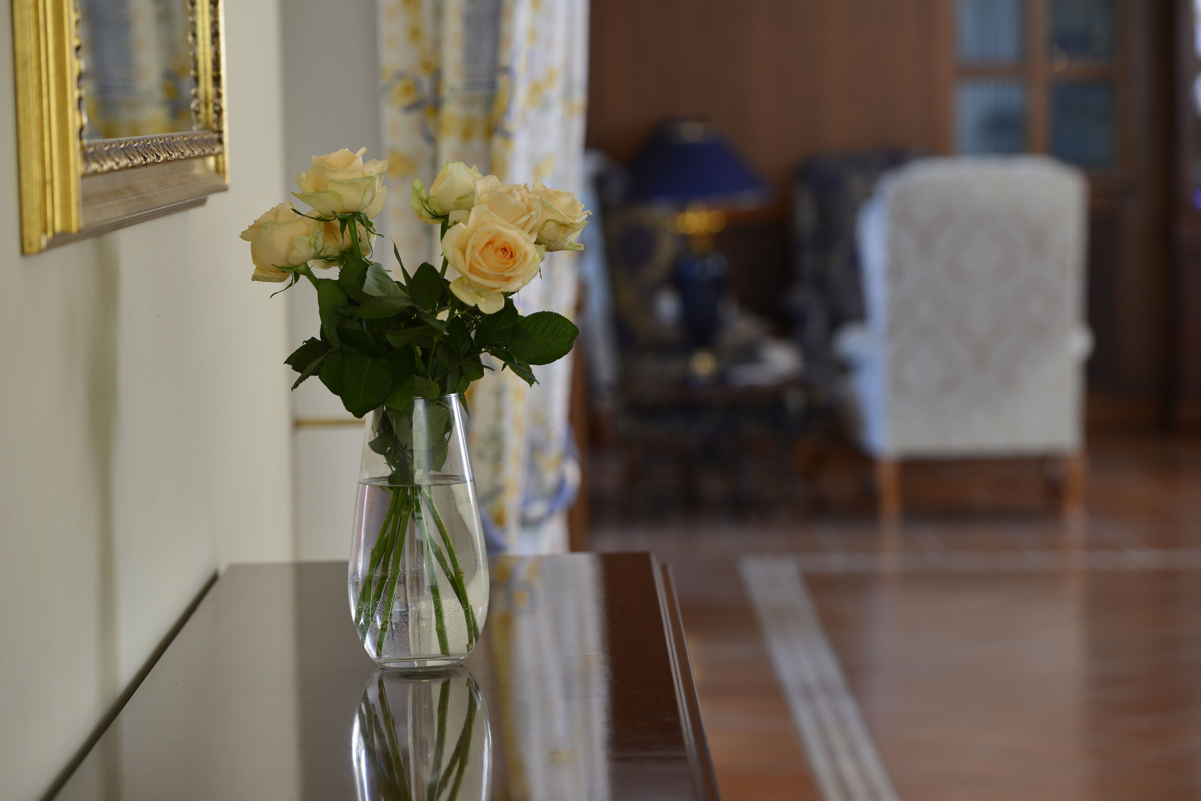 A vase with flowers on a table in a room with a mirror and a lamp.