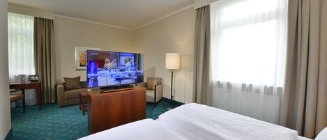 A hotel room with a bed, a desk with a computer, a television, and a lamp.