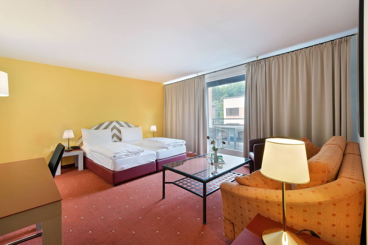 A hotel room with a bed, a sofa, a table, and a lamp.