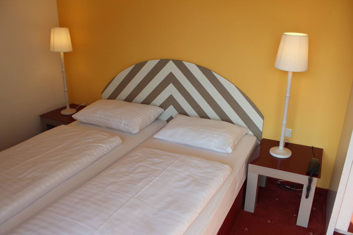 A double bed with a chevron-patterned headboard, two bedside lamps, and a small table with a lamp.