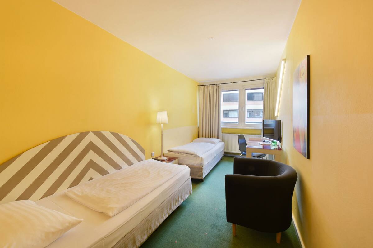 A hotel room with two beds, a desk, a chair, and a window with curtains.