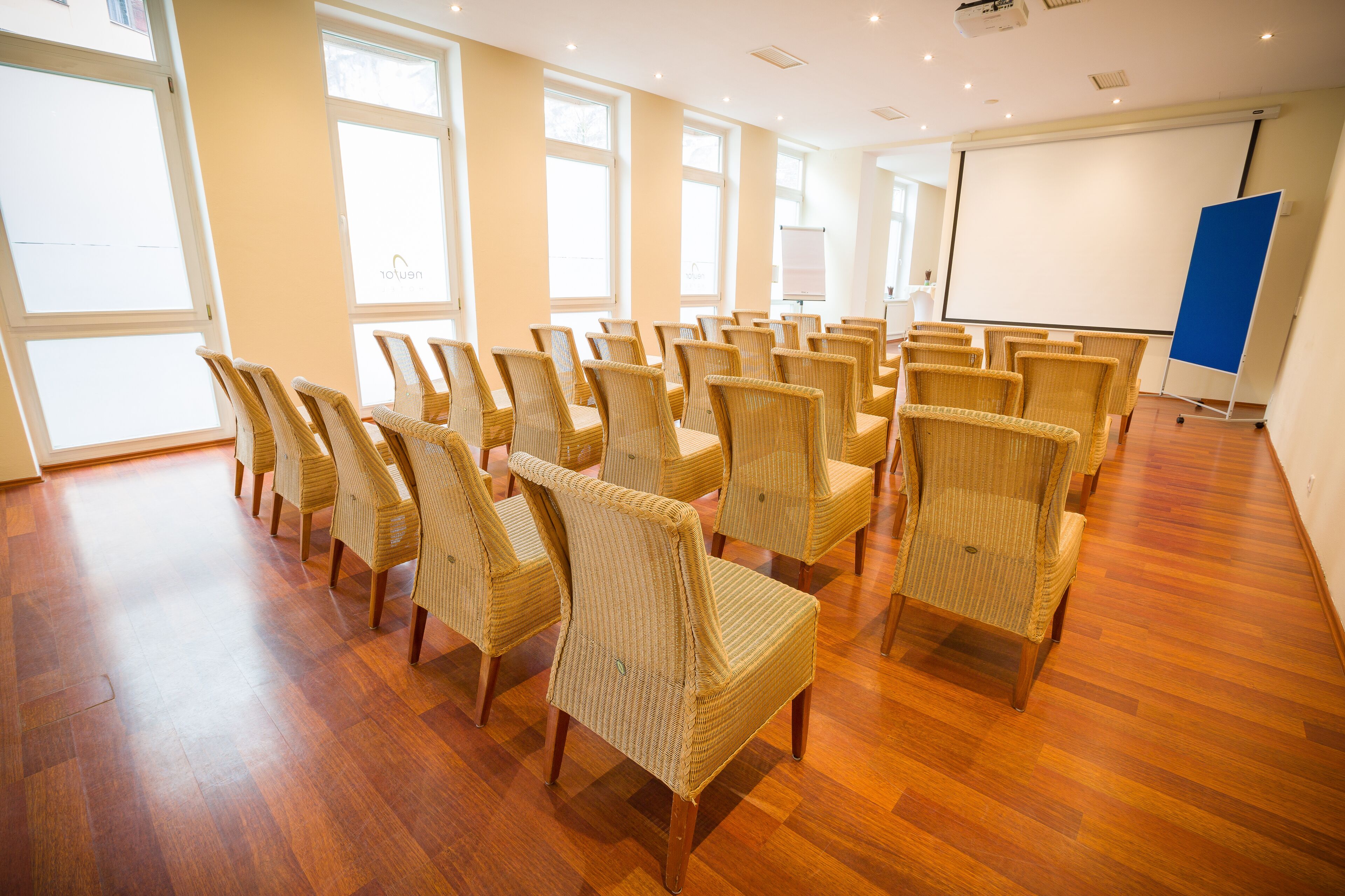Een vergaderzaal met rieten stoelen in rijen, een whiteboard en een projectiescherm.
