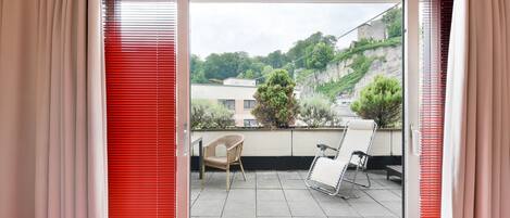 A balcony with a view of a hillside, a wicker chair, and a metal chair.