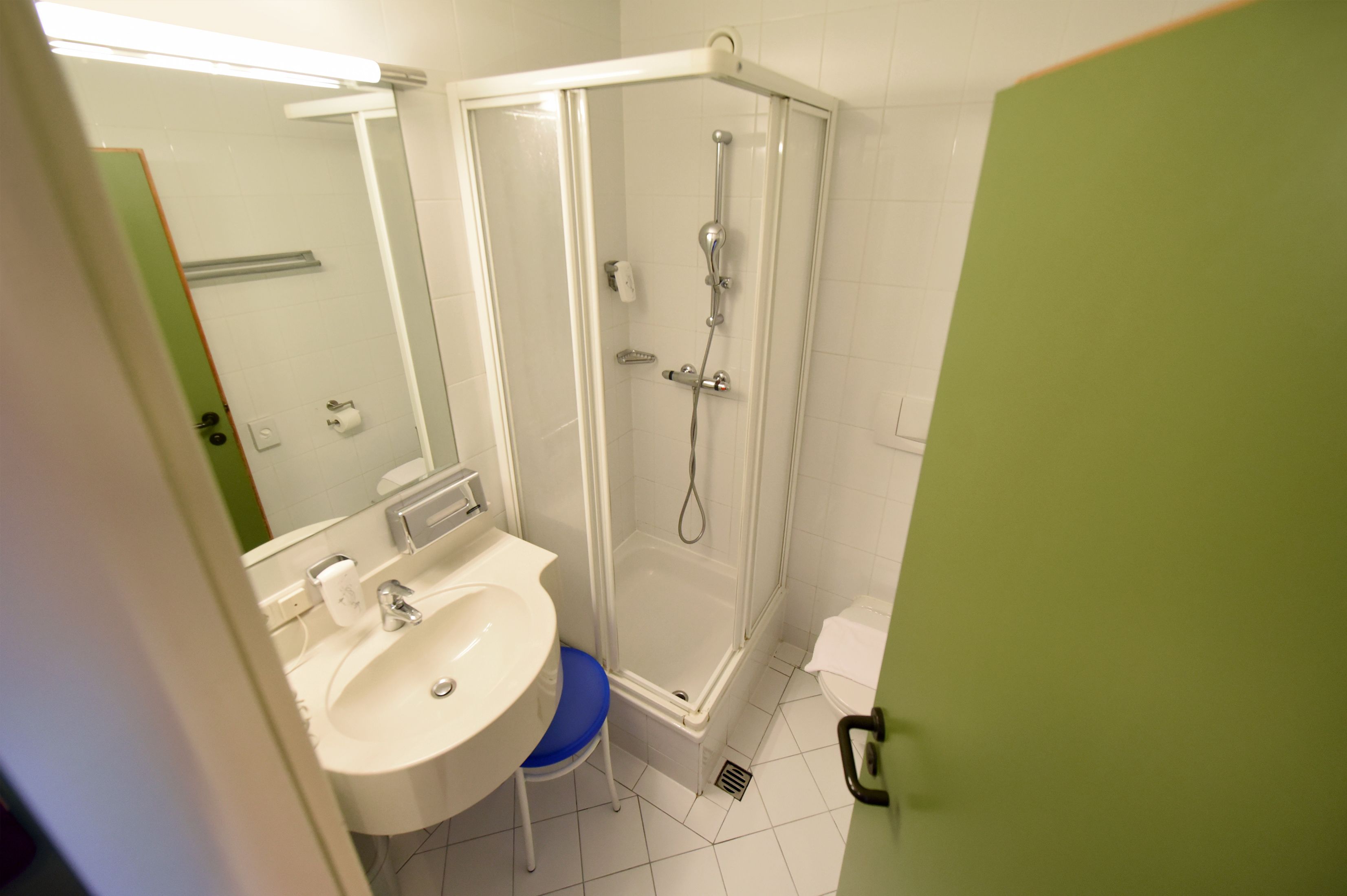 Un baño con un lavabo blanco, cabina de ducha con mampara de vidrio y una puerta verde.