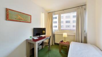 Ein Hotelzimmer mit Bett, Schreibtisch, Stuhl, Fernseher, Lampe und einem Bild an der Wand.