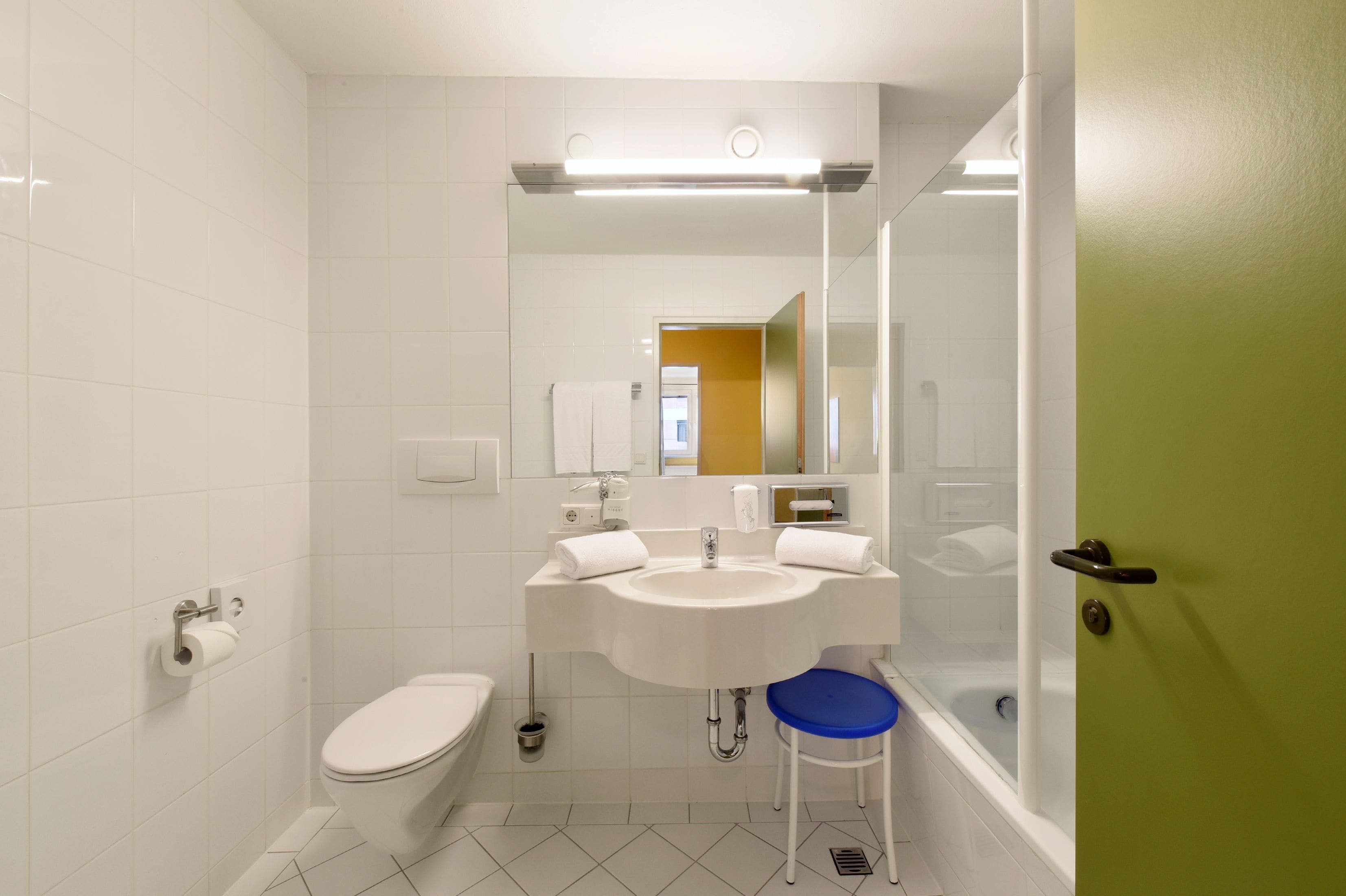 Ein Badezimmer mit Waschbecken, Toilette und blauem Hocker.