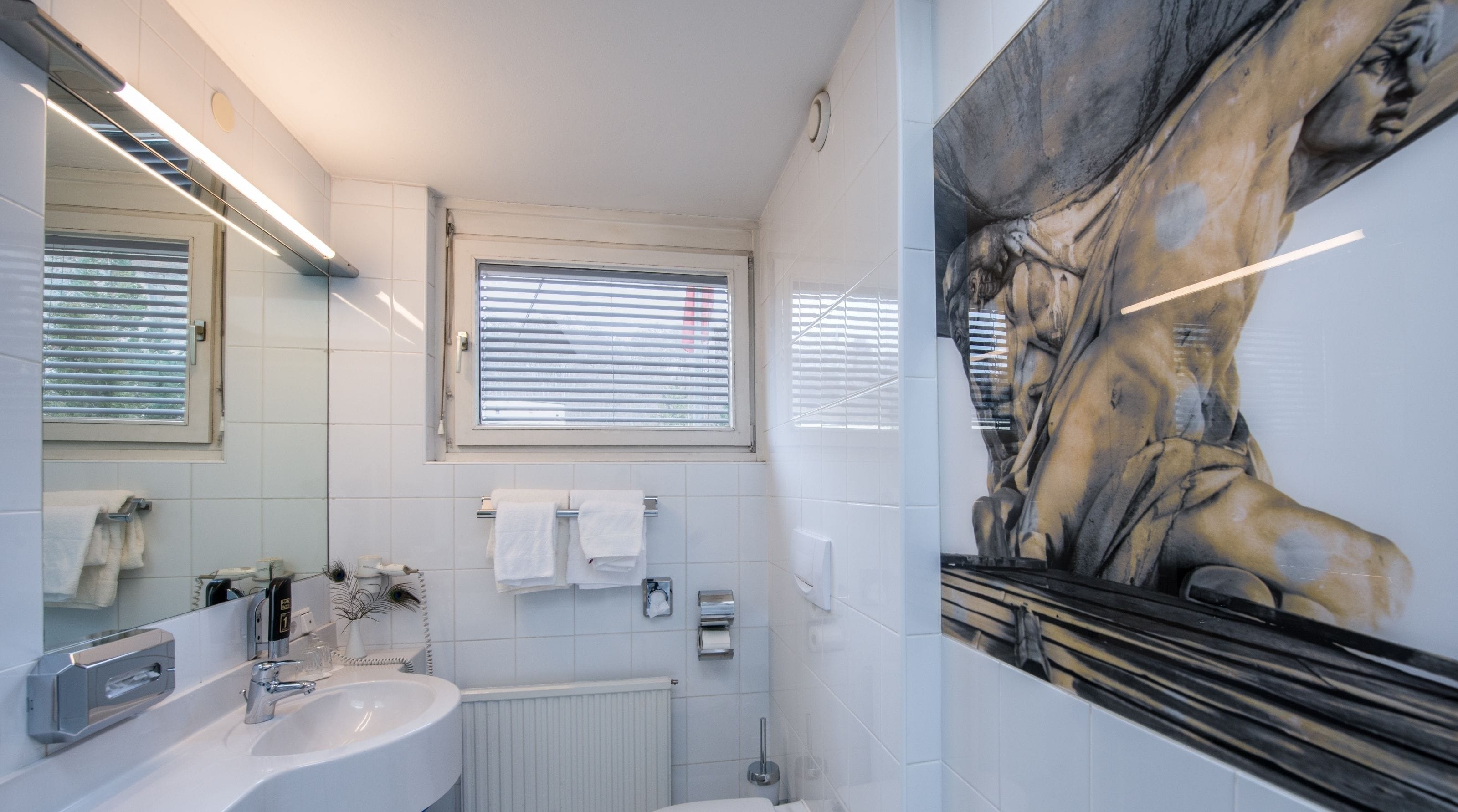 A modern bathroom with a large mirror, white tiles, a sink, and a window with blinds.