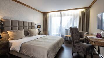 A hotel room with a large bed, a desk, a chair, a lamp, and a television.