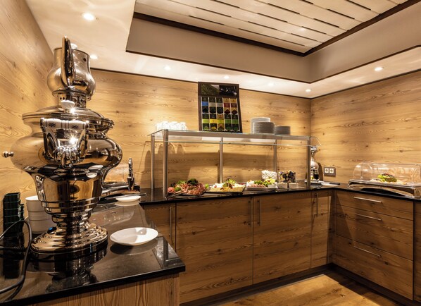 Una cocina moderna con una cafetera de acero inoxidable, una vitrina con alimentos, armarios de madera e iluminación empotrada en el techo.
