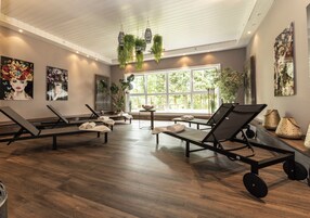 A spa room with multiple massage tables, large windows, and indoor plants.
