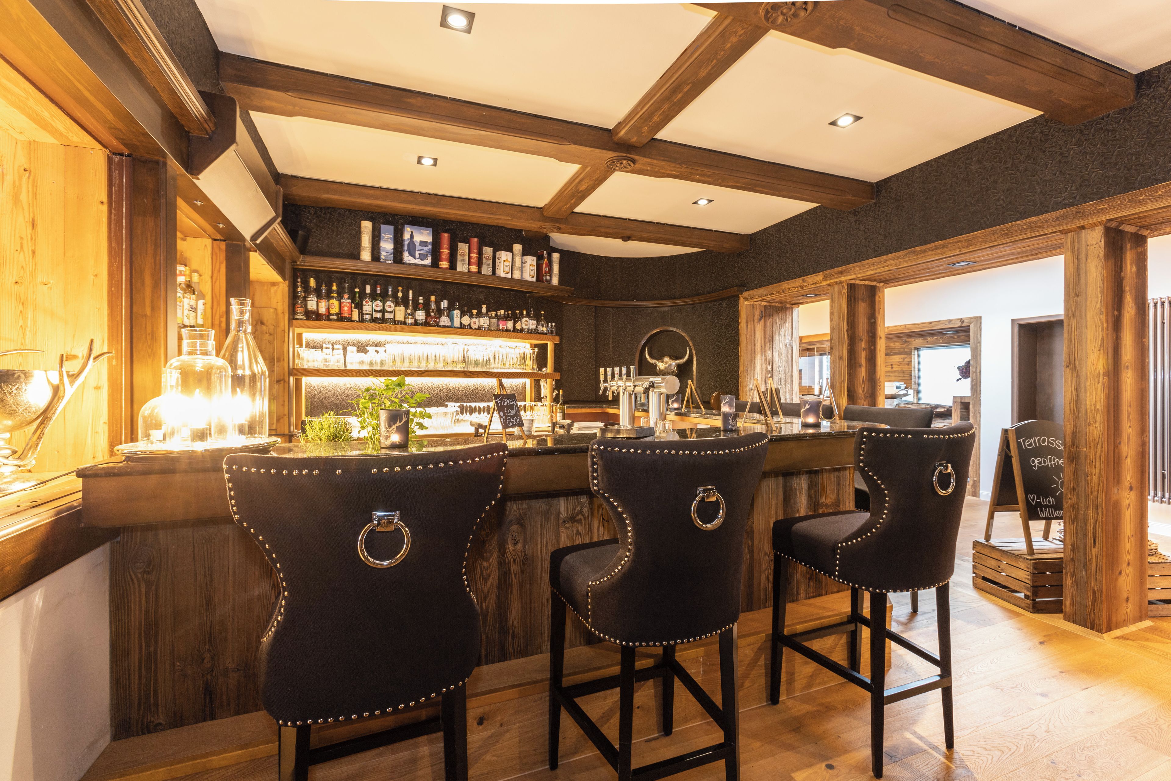 Zona de bar con taburetes de madera y una estantería de botellas de licor.