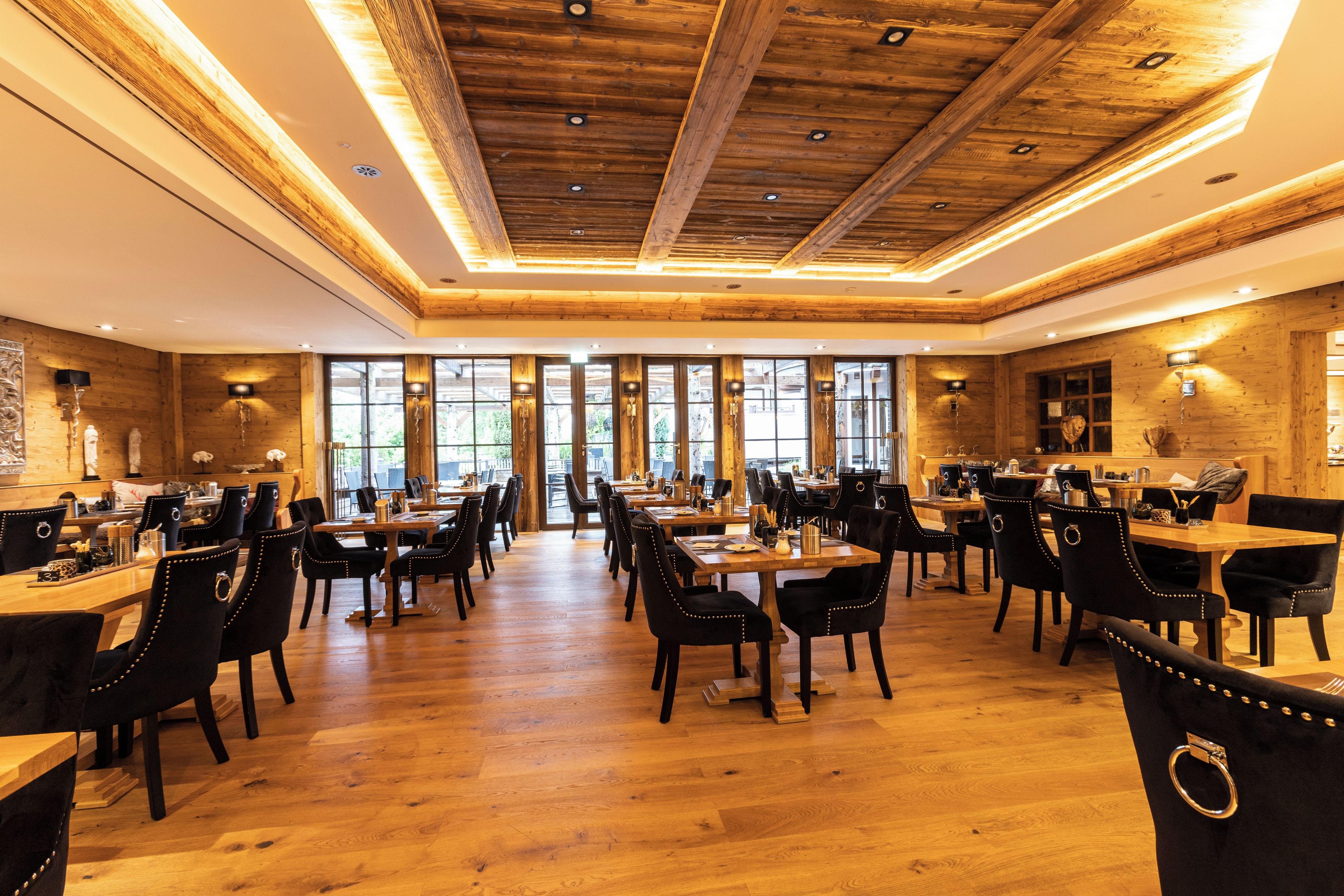 A spacious dining area with wooden flooring, multiple tables, and chairs.