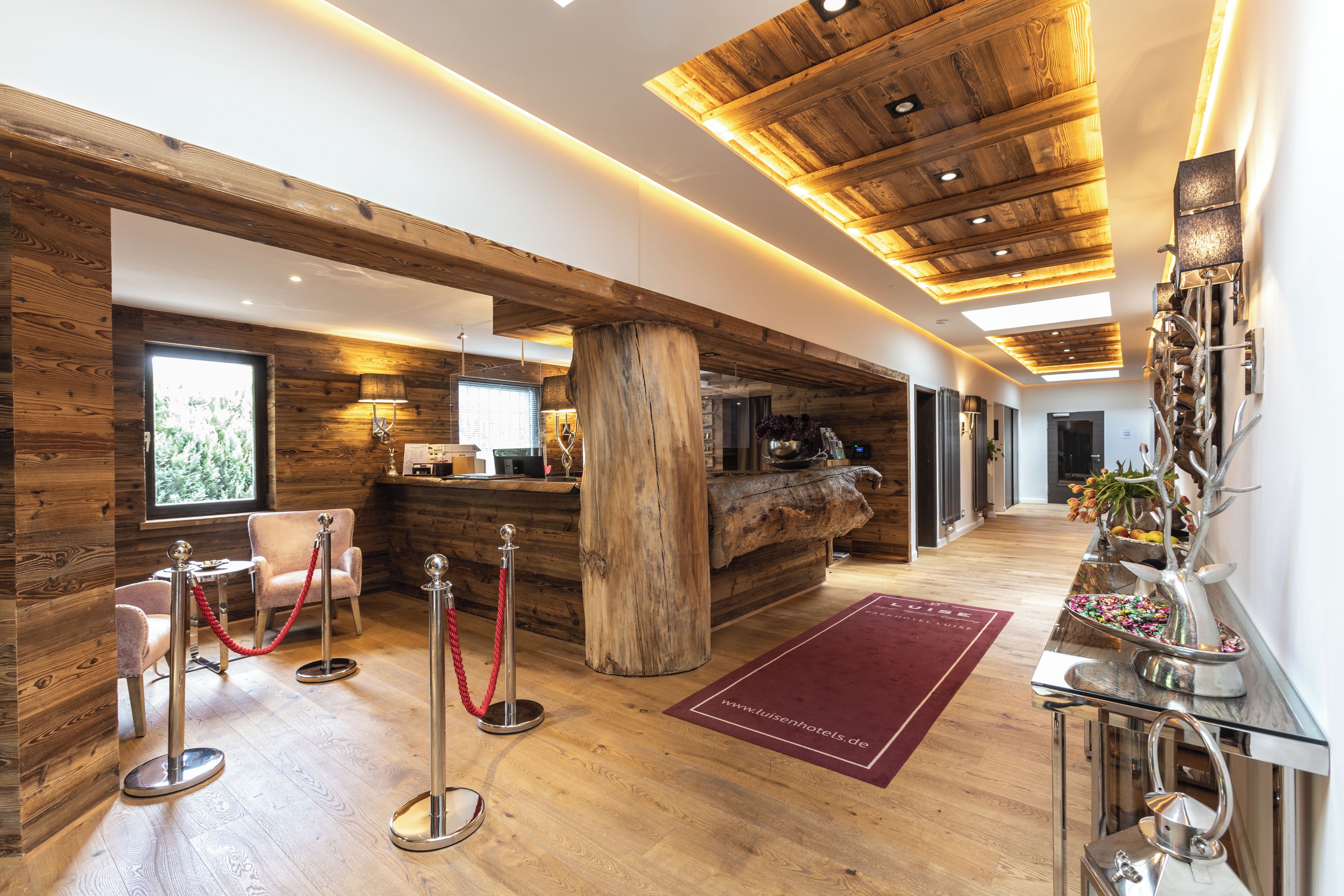 Un hall d’hôtel avec des panneaux de bois, un comptoir d’accueil, un grand tronc d’arbre et un tapis rouge.