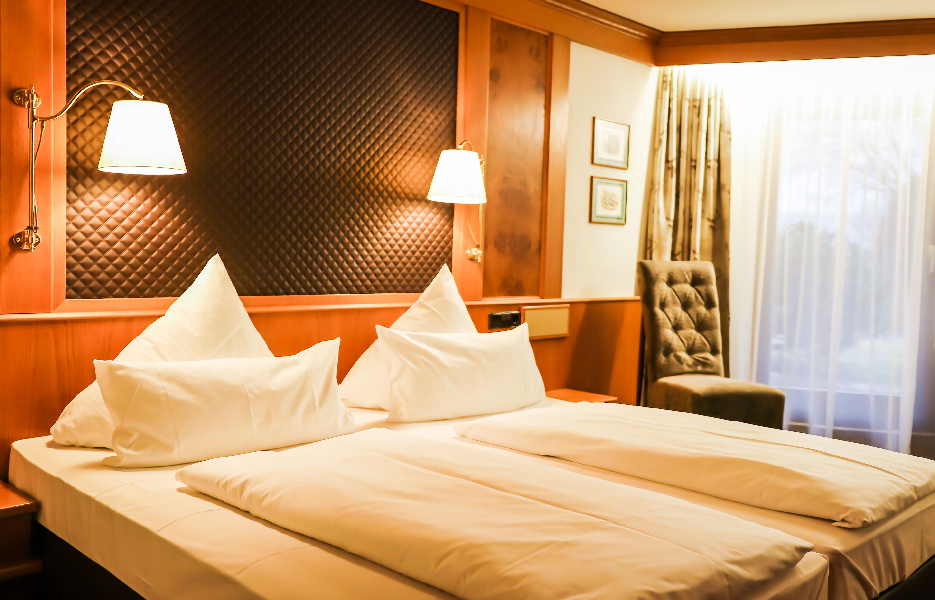 Habitación de hotel con una cama grande, dos lámparas de noche, una silla y una ventana con cortinas.