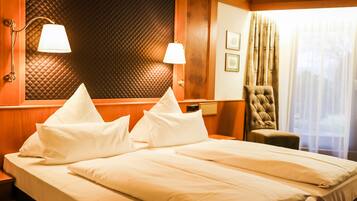 Habitación de hotel con una cama grande, dos lámparas de noche, una silla y una ventana con cortinas.