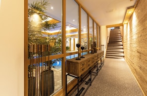 A modern interior with a wooden staircase, a long wooden bench with drawers, and a glass wall overlooking a pool area. - Waldhotel Luise (Freudenstadt)