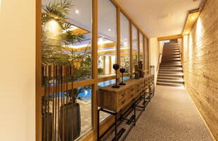 A modern interior with a wooden staircase, a long wooden bench with drawers, and a glass wall overlooking a pool area.