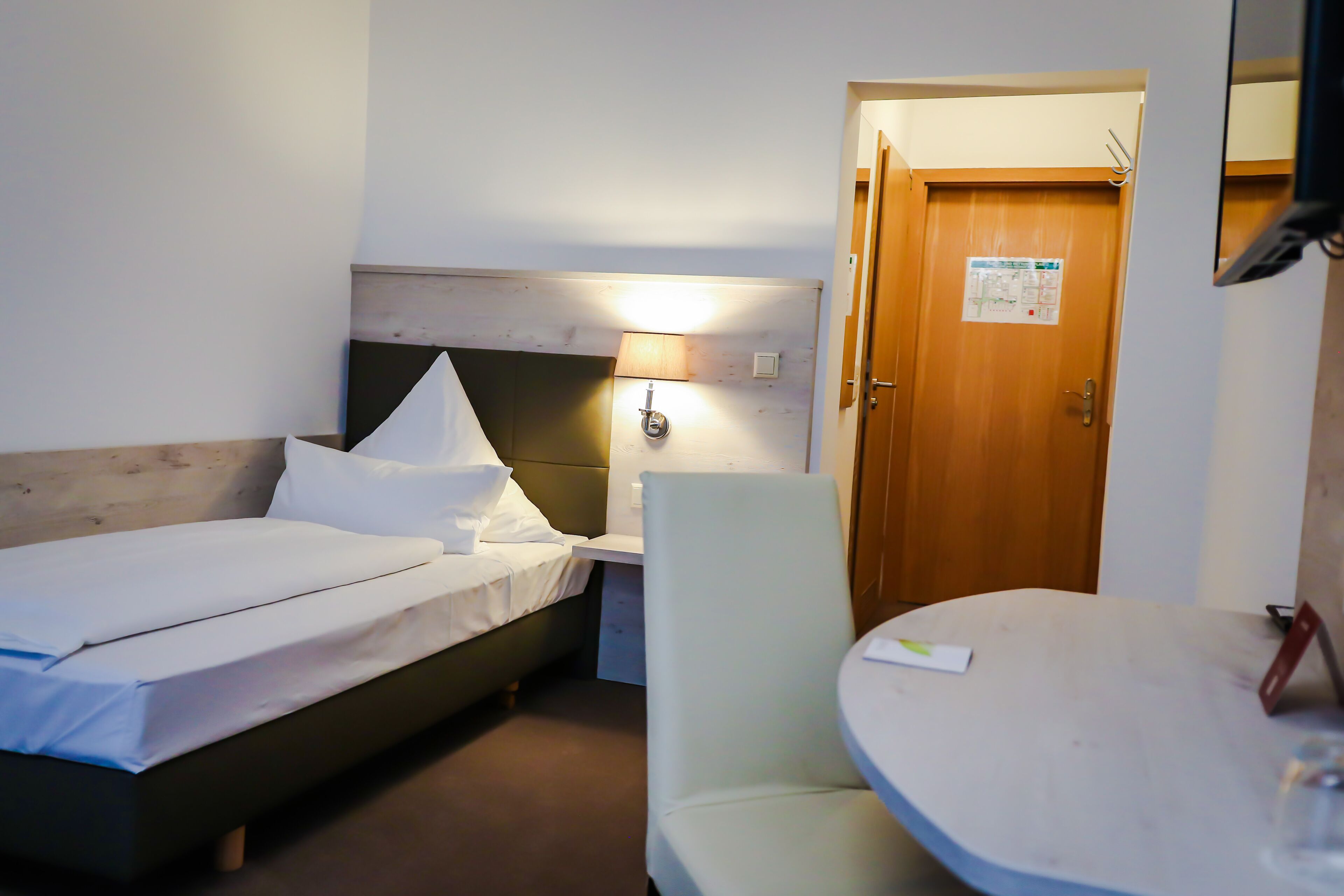 Ett hotellrum med en säng, ett skrivbord, en stol och en dörr.