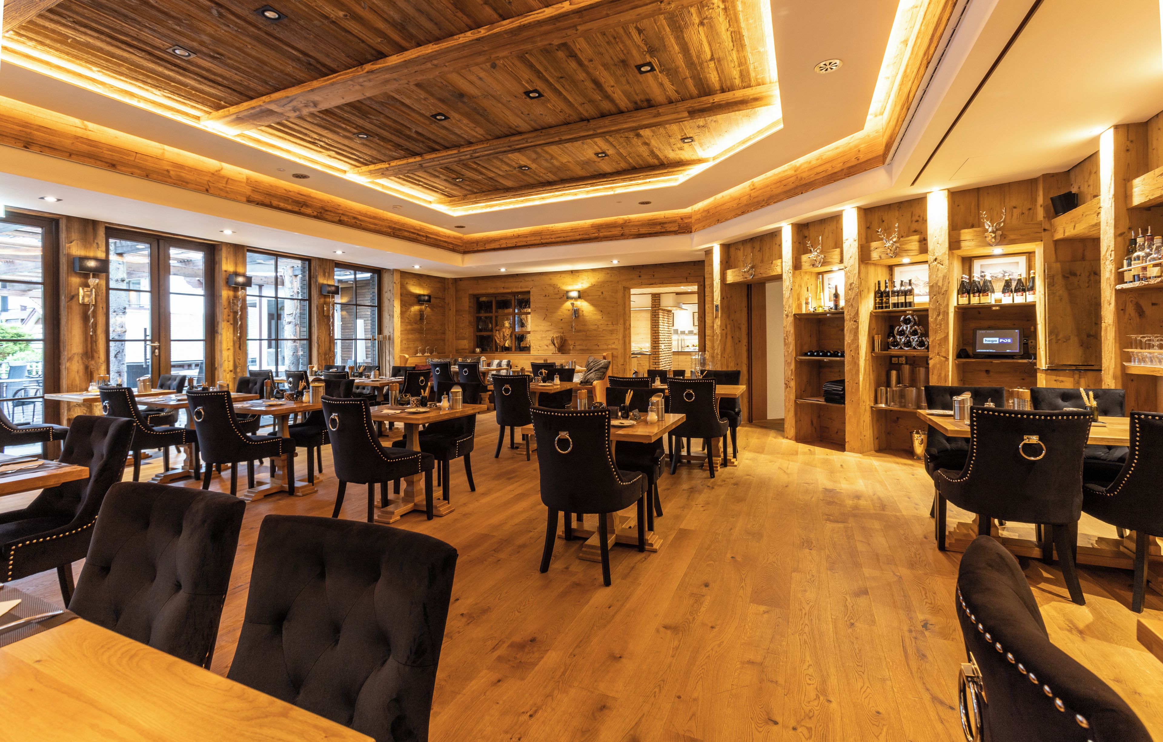 Un restaurante con techo y paredes de madera, varias mesas de comedor con sillas, y una zona de bar con estantes llenos de botellas.