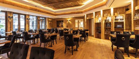 Un restaurante con techo y paredes de madera, varias mesas de comedor con sillas, y una zona de bar con estantes llenos de botellas.