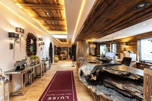 Un interior moderno con vigas de madera en el techo, una recepción con un mostrador de madera maciza y una alfombra roja que guía hacia la entrada.
