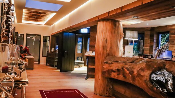 A spacious lobby with a wooden reception desk, a large wooden column, and a red carpet. - Waldhotel Luise (Freudenstadt)