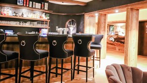 A bar area with wooden beams, black bar stools with gold rings, and a variety of bottles and glasses on shelves. - Waldhotel Luise (Freudenstadt)