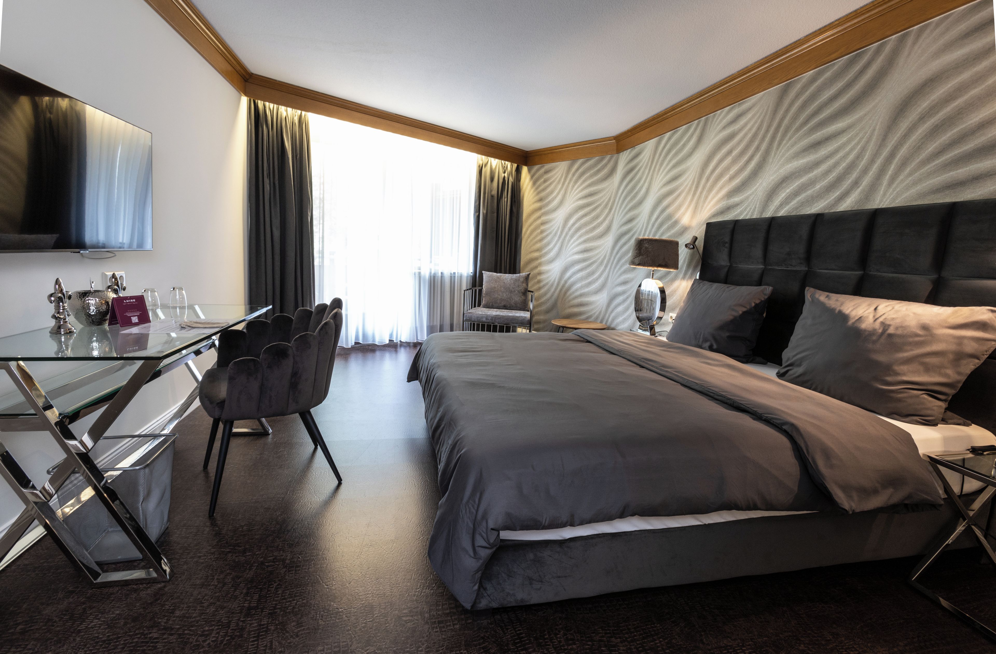 A modern hotel room with a large bed, a desk, a chair, and a television.