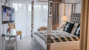 A modern hotel room with a four-poster bed, a glass desk, and a television displaying a video. - Waldhotel Luise (Freudenstadt)