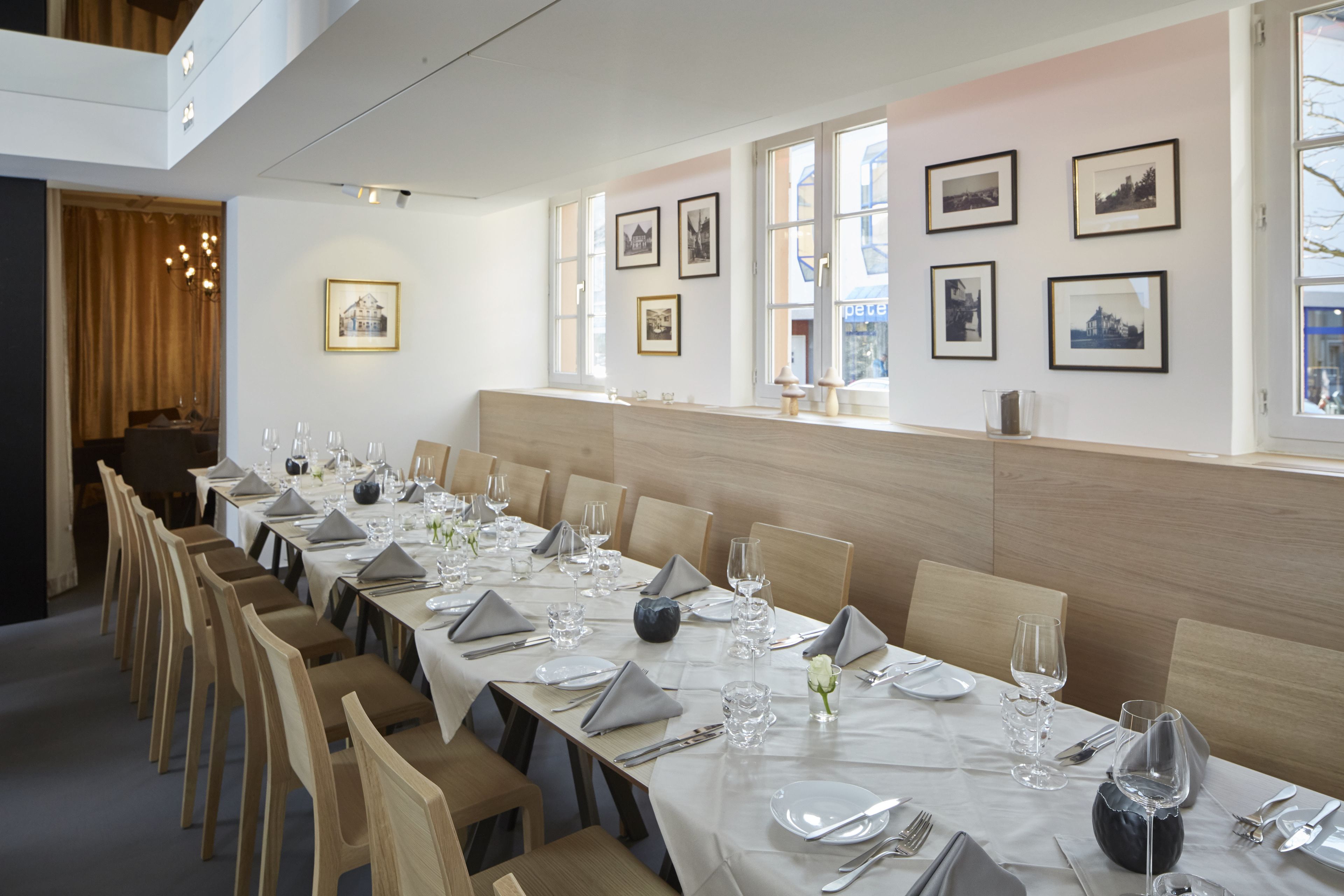Una larga mesa de comedor dispuesta con sillas, cuadros en la pared y un ventanal con vistas.