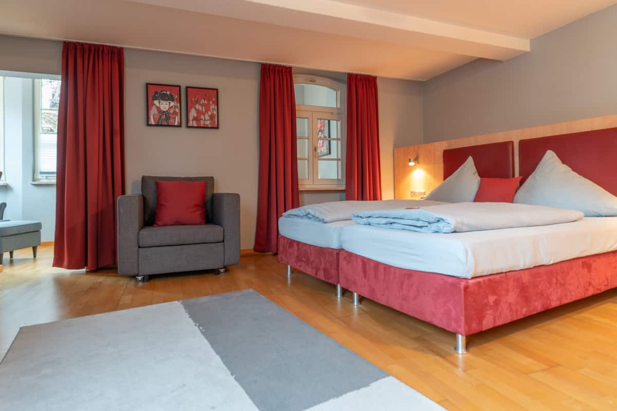 Un dormitorio con cama, sofá, ventana y mesita de noche.