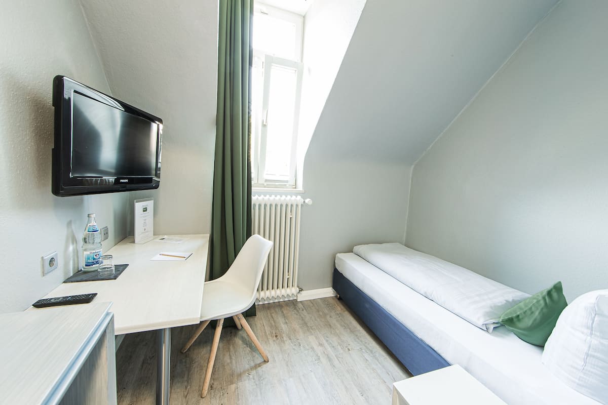 Una habitación pequeña y moderna con una cama, un escritorio, una silla, un televisor y una ventana con cortinas.