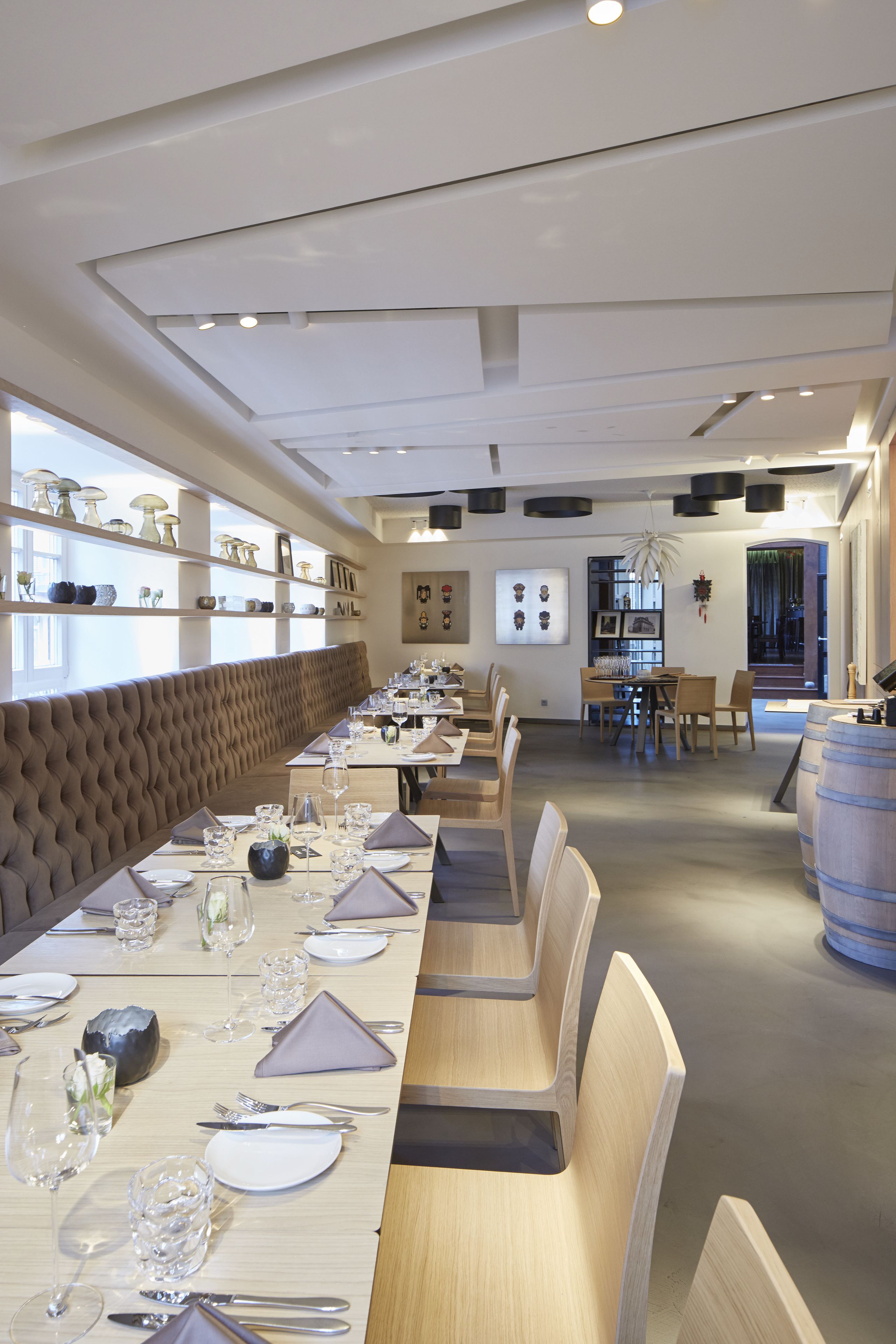 Un restaurante con una larga mesa de madera preparada para comer, un banco acolchado a lo largo de la pared y estantes con objetos decorativos.