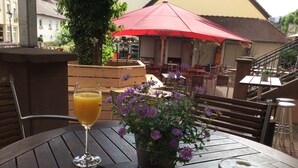 Ein Tisch mit einer Zeitschrift, einem Orangensaftglas, einer Kaffeetasse und einem Topf mit violetten Blumen.