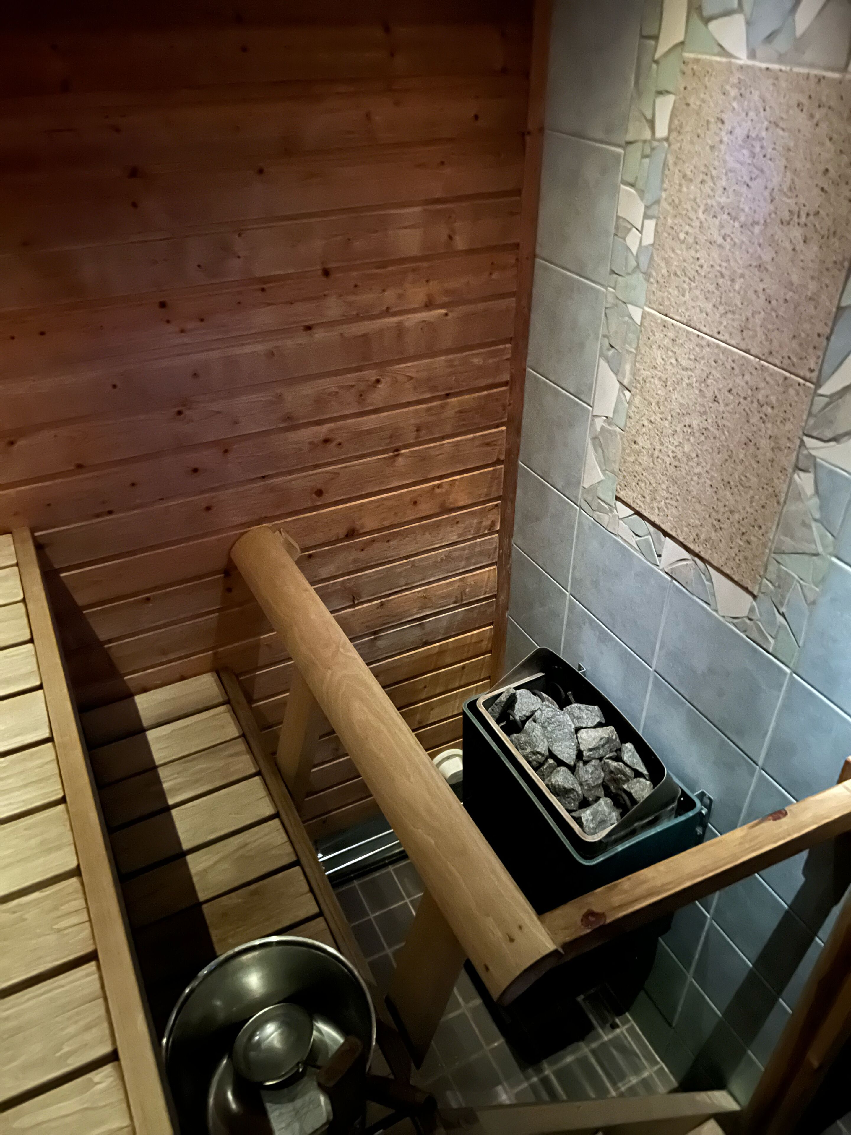 Interno di una baita di legno con un secchio di metallo, una panca in legno e una scatola di carbone.