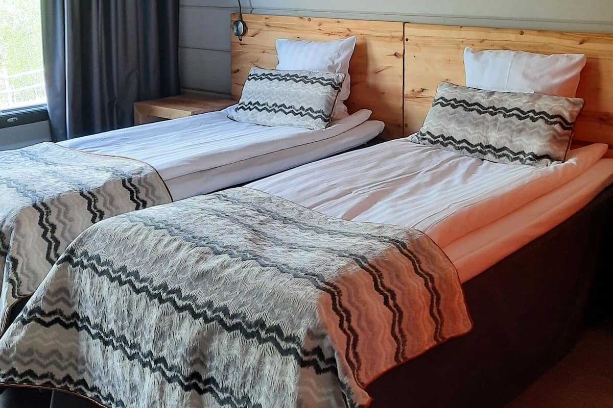 A double bed with two pillows, a wooden headboard, and a window with curtains.