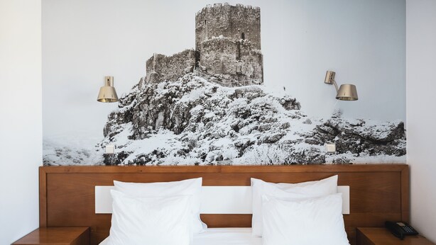 A hotel room with a large bed, wooden headboard, two bedside tables, and a wall-mounted lamp. - Hotel Rural Senhora De Pereiras (Vimioso)