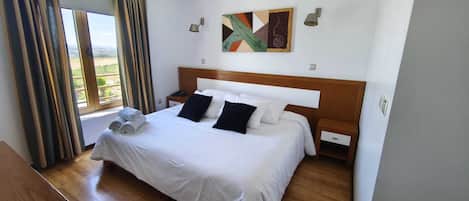 Une chambre d’hôtel avec un grand lit, une tête de lit en bois, un tableau au mur et une fenêtre avec des rideaux.