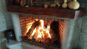 A fireplace with a fire burning inside, surrounded by a stone wall and a wooden mantelpiece above it.