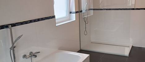 A modern bathroom with a bathtub, shower, and a window.
