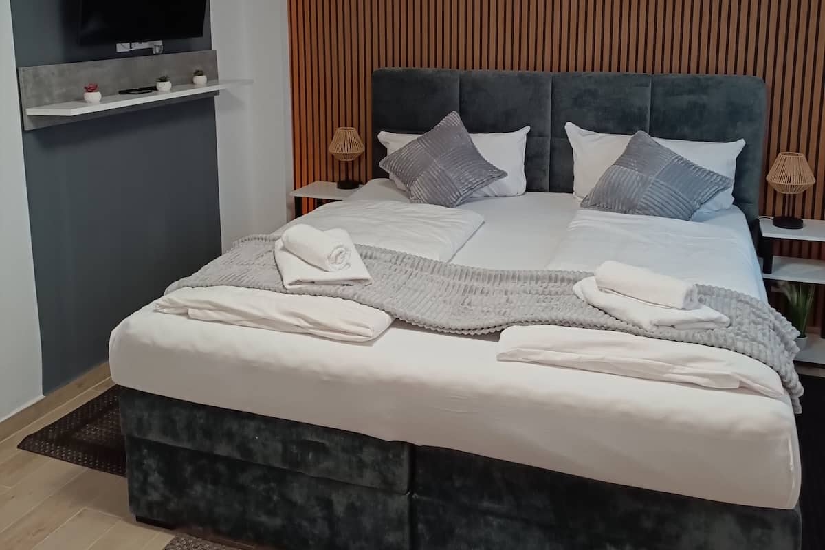 Une chambre à coucher moderne avec un grand lit, un téléviseur à écran plat fixé au mur et une tête de lit en lattes de bois.