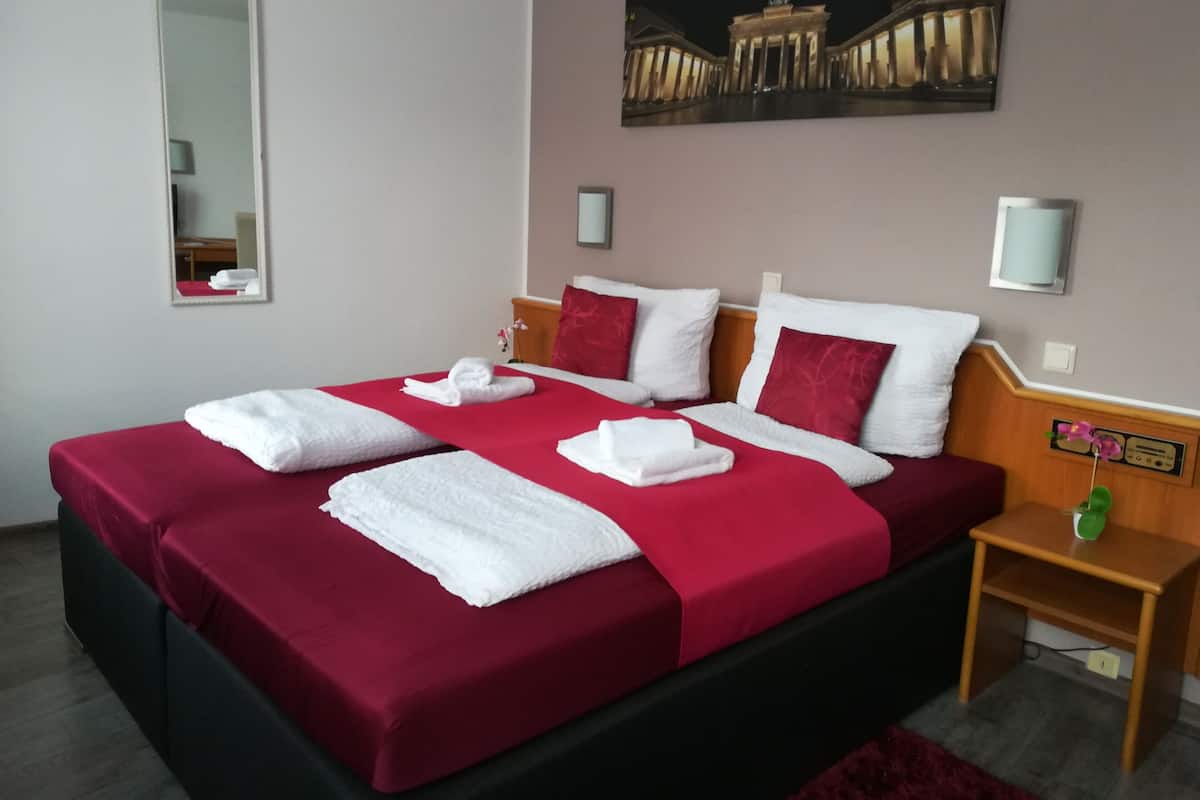Une chambre d’hôtel avec un grand lit, une literie rouge, des oreillers blancs et un tableau représentant un bâtiment accroché au mur.