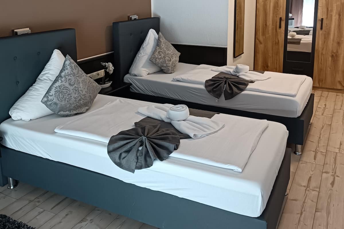 Une chambre d’hôtel avec deux lits, un tableau représentant une cascade et une armoire en bois.