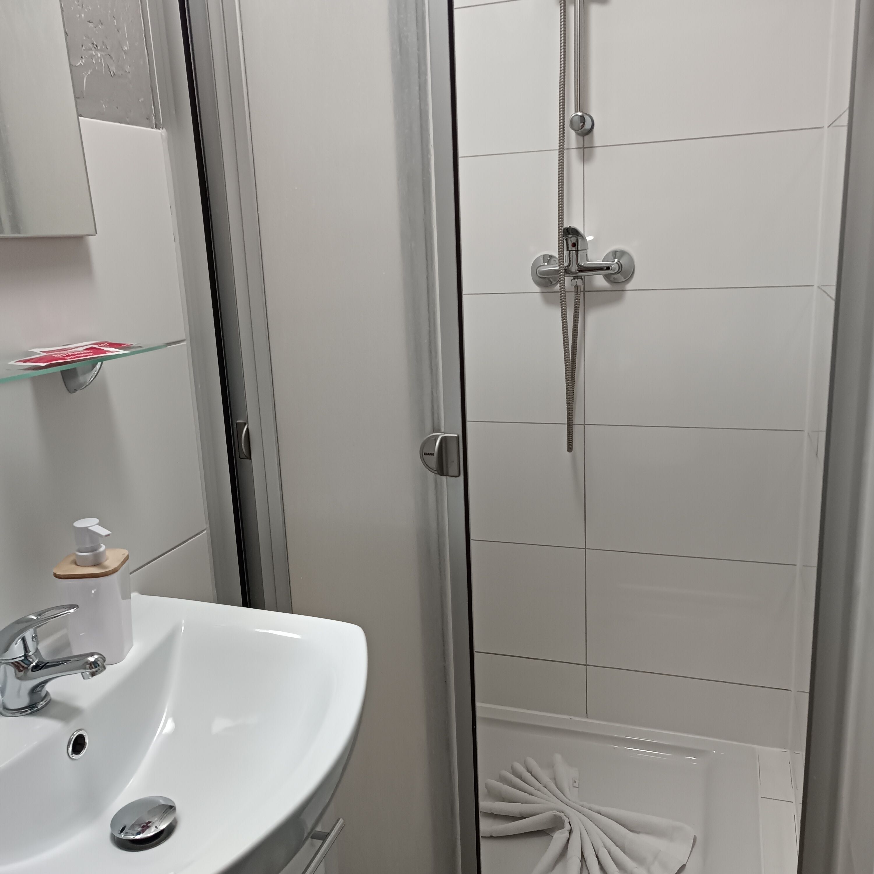 A bathroom with a white sink, a glass shelf with toiletries, and a shower with a handheld showerhead.