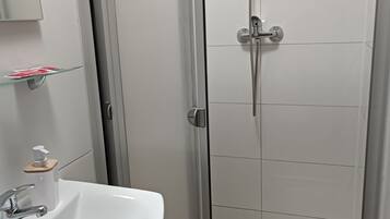 A bathroom with a white sink, a glass shelf with toiletries, and a shower with a handheld showerhead.