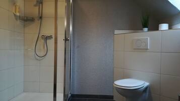A modern bathroom with a glass-enclosed shower, a toilet, and a small plant on the wall.